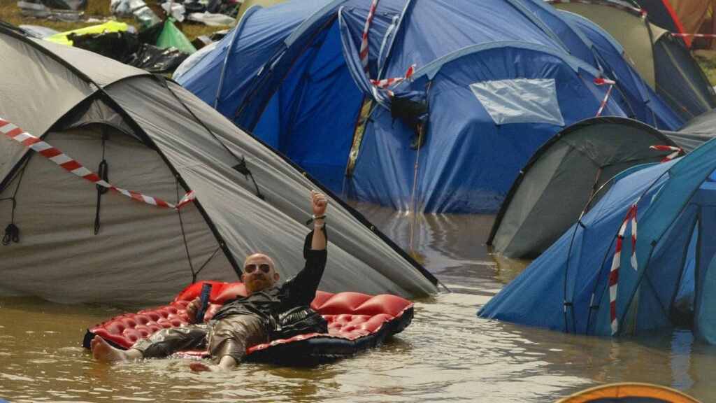 Festival goer making the best of a flooded camping area floating on an inflatable air mattress like a raft