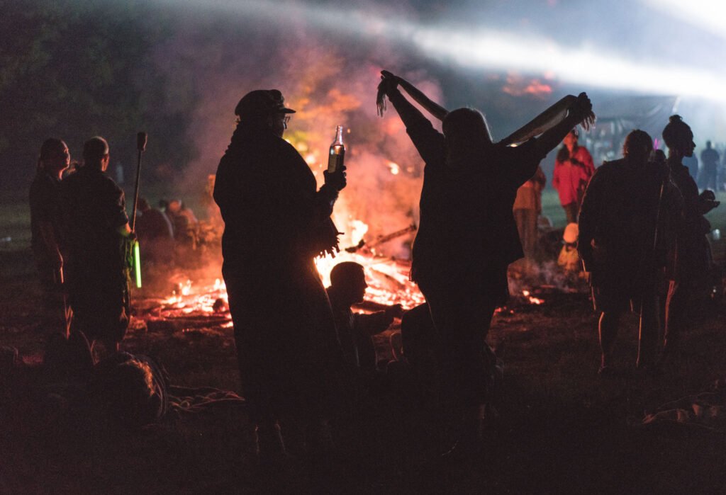 Festival goers with pashminas and scarves standing around a large bon fire at Peace Fest music festival